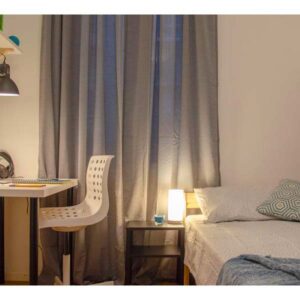 panoramica della stanza con letto singolo, comodino, zona studio con scrivania sedia e lampada, letto singolo