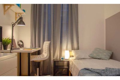 panoramica della stanza con letto singolo, comodino, zona studio con scrivania sedia e lampada, letto singolo
