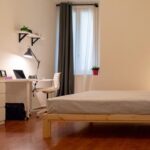 dettaglio della stanza con vista su letto matrimoniale, zona studio con scrivania, lampada e sedia, e finestra