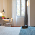 dettaglio della stanza, con scrivania, sedia ergonomica e una finestra che si affaccia sul viale