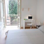 vista del letto matrimoniale e della zona studio lavoro con balcone aperto che si affaccia su alberi