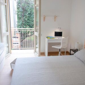 vista del letto matrimoniale e della zona studio lavoro con balcone aperto che si affaccia su alberi