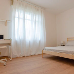 vista ampia della stanza, con letto, scrivania e una finestra molto luminosa